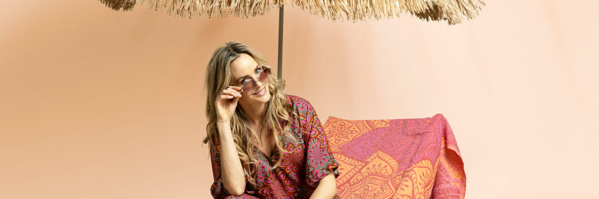 Frau in Paisley-Sommerkleidung unter Strohschirm am Strand